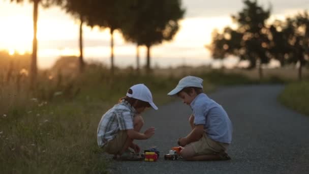Två barn, pojke bröder, att ha kul på en med leksaksbilar på sunset — Stockvideo