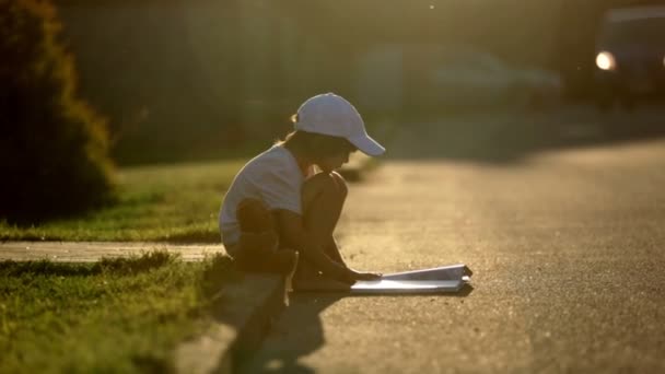 Beautiful kid boy, reading a book on the street, sitting down with teddy bear, gorgeous sunset light — Stock Video