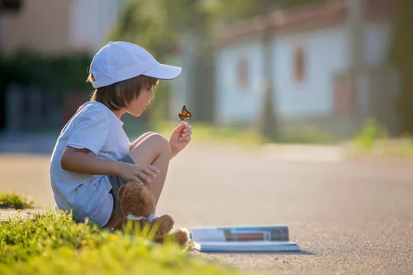 Beautiful kid boy, reading a book on the street, sitting down wi — Stock Photo, Image