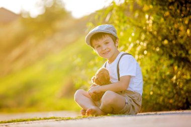 Tatlı çocuk, oyuncak ayı güneşler bir küçük kırsal yolda ile oynarken