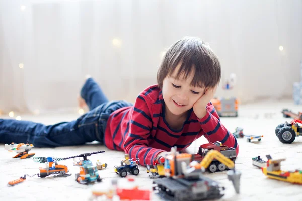 Pequeño niño jugando con un montón de juguetes de plástico de colores en interiores —  Fotos de Stock