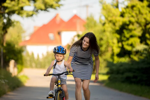 Young mother, helping her son to learn how to ride a bike, holding him and teaching him biking