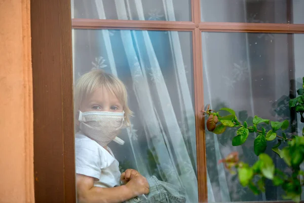 小さな幼児の子供 男の子 窓のシールドに悲しい座って 日没を見て 保護医療マスクを着て コロナウイルスのために隔離された — ストック写真