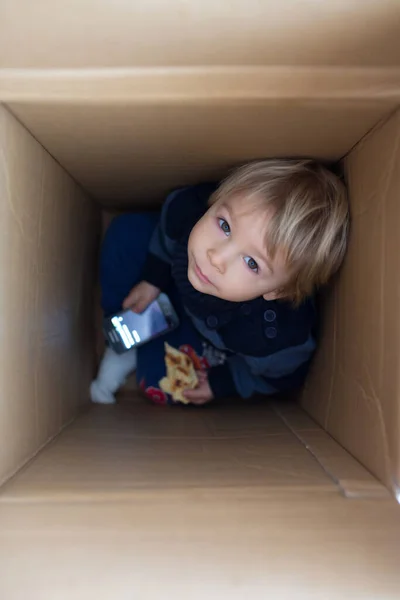 Stock image Sweet toddler child, cute blond boy, hiding in cardboard box, looking out from a hole, smiling