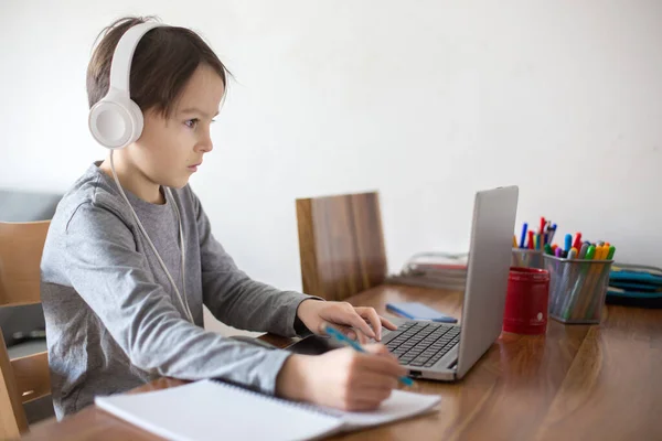 学校はコロナウイルスのため閉鎖されている間 学校の子供は ノートパソコンでテーブルに座って 学校のタスクを書き込みます — ストック写真