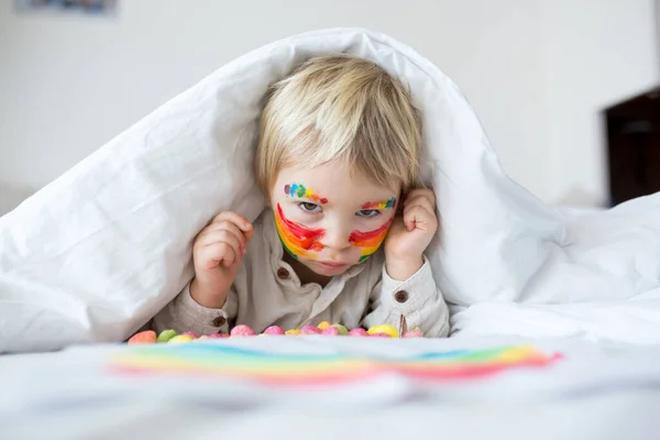 美しいですブロンド幼児男の子とともに虹彩塗装彼の顔と乱雑な手 幸せな笑顔 — ストック写真
