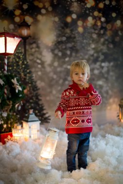 Tatlı sarışın çocuk, kırmızı kazaklı, ormanda fener tutan, Noel zamanı, kar yağıyor.