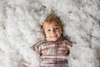 Şirin çocuk, elinde örgü bir oyuncak, renkli kardan adamlarla karda oynuyor, mutlu bir şekilde gülümsüyor.