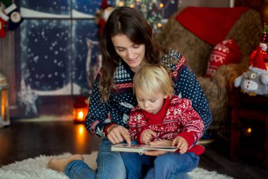 Mutlu gülümseyen bir aile, anne ve çocuk, Noel tatillerinde kitap okuyor.