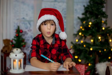 Sevimli küçük çocuk Noel dekorasyonu çevresindeki evde, Noel Baba'ya mektup yazma ahşap bir masaya oturup, 