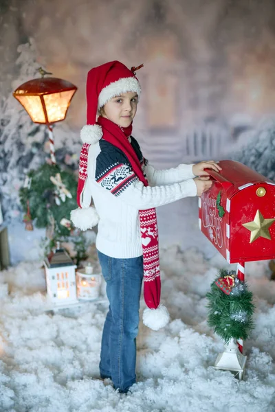 かわいい子供 学校の男の子 クリスマスのメールボックスでサンタに手紙を送る 彼の周りのクリスマスの装飾 屋外のショット 屋外の雪のショット — ストック写真