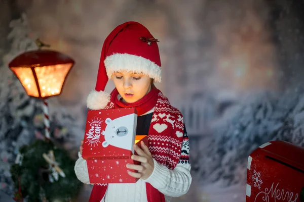 かわいい子供 学校の男の子 クリスマスのプレゼントを開く 彼の周りの装飾 屋外のショット 屋外の雪のショット — ストック写真