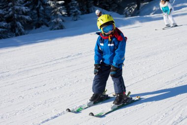 Şirin küçük bir çocuk, Avusturya 'daki dağlarda kayak merkezinde kışın mutlu bir şekilde kayak yapıyor.