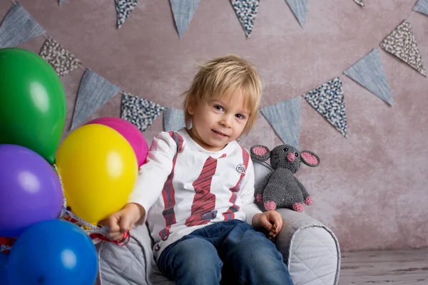 可爱的金发碧眼的小孩 坐在小孩的小扶手椅上 玩着五颜六色的气球 开心地笑着 在室内射击 — 图库照片