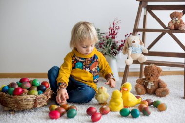 Küçük çocuk, sarışın çocuk paskalya yumurtalarıyla oynuyor. Çocuklar evde yumurta ve civcivlerle oynuyorlar.