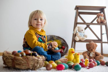 Küçük çocuk, sarışın çocuk paskalya yumurtalarıyla oynuyor. Çocuklar evde yumurta ve civcivlerle oynuyorlar.
