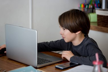 Üzgün okul çocuğu, çalışmayla boğuşuyor, dizüstü bilgisayarla masada oturuyor, evde eğitim görürken okul ödevleri yazıyor, salgın dinamiği öğretiyor.