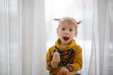 Tatlı bir çocuk, at kuyruklu küçük bir bebek, evde aylaklık ediyor, dondurma yiyor, komik suratlar yapıyor ve gülümsüyor.