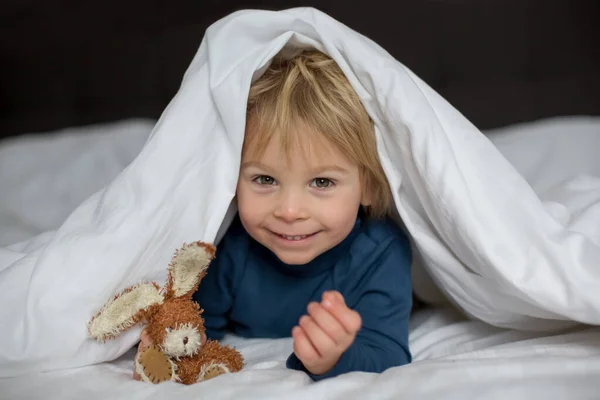 かわいい子がベッドに横になって小さなおもちゃで遊んで幸せそうに笑って — ストック写真