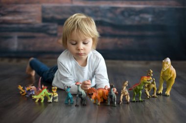 Sarışın küçük çocuk, evde dinozorlarla oynuyor, hoş bir sırt lambası.