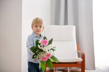 Güzel sarışın çocuk, güneşli oturma odasında anneler günü için küçük hediyeler vererek annesine çiçek ve kutu veriyor.