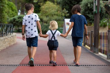 Children, boy brothers, siblings holding hands and crossing crosswalk on the street, summertime