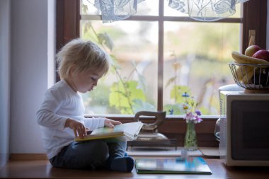 Küçük çocuk, sabahları mutfakta kitap okuyor.