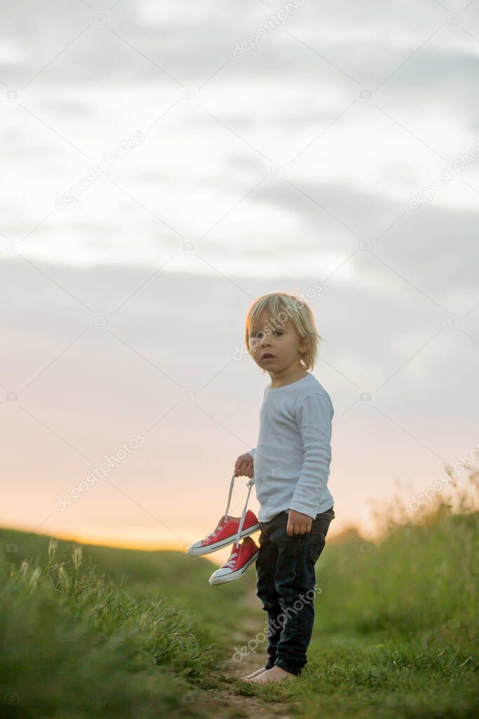 Happy child, holding pair of sneakers in hands, walking on a rural path, barefeet