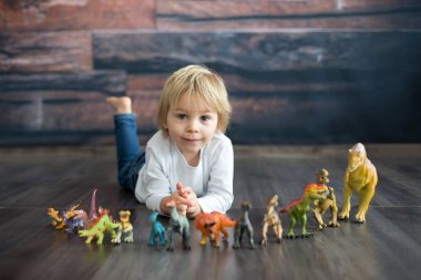 Sarışın küçük çocuk, evde dinozorlarla oynuyor, hoş bir sırt lambası.