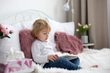 Tatlı çocuk, yatakta uzanıyor, evde kitap okuyor.