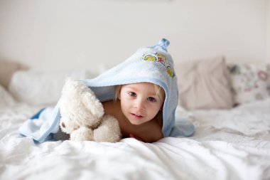 Küçük tatlı sarışın çocuk, banyodan sonra yatakta dinleniyor, mutlu bir şekilde gülümsüyor, gündüz vakti.