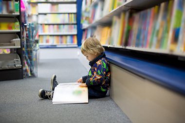 Bir kitapçıda oturup kitap okuyan sevimli küçük bir çocuk.