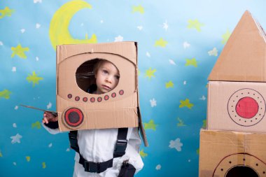 Tatlı çocuk, astronot gibi giyinmiş, evde karton roket ve kutudan yapılmış el yapımı kaskla oynuyor.