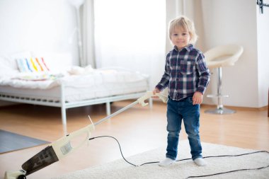 Sevimli küçük bebek, çocuk, evdeki oturma odasında elektrikli süpürge.