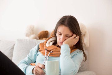 Yorgun anne, yeni doğmuş çocukla uykusuz bir geceden sonra bir fincan kahveyle kanepede oturuyor.