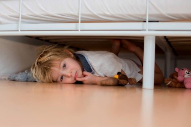 Küçük çocuk, doldurulmuş oyuncaklarla yatağın altında saklanıyor, kabus canavarlarından korkuyor.