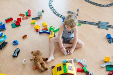 Sevimli çocuk, renkli oyuncak bloklarıyla oynuyor. Güneşli, ferah yatak odasında yerde oturan küçük çocuk oyuncaklardan ev inşa ediyor. Bebekler için eğitici bir oyun