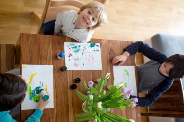 Çocuklar, kardeşlerim, evde akvaryum boyalarıyla resim çiziyorlar, yukarıdan çekilmiş.