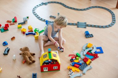 Sevimli çocuk, renkli oyuncak bloklarıyla oynuyor. Güneşli, ferah yatak odasında yerde oturan küçük çocuk oyuncaklardan ev inşa ediyor. Bebekler için eğitici bir oyun