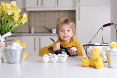 Küçük çocuk, siyah kalemle paskalya yumurtalarına komik ifadeler çiziyor.