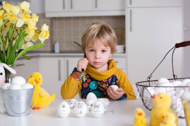 Küçük çocuk, siyah kalemle paskalya yumurtalarına komik ifadeler çiziyor.