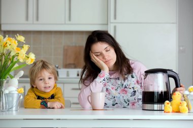 Yorgun anne, sabahları kahve koymaya çalışıyor. Uykusuz bir geceden sonra mutfak masasında uzanmış kahve içmeye çalışan bir kadın.