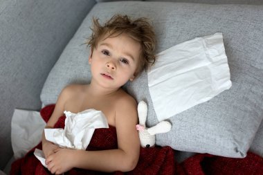 Küçük çocuk, çocuk, kanepede hasta yatıyor, annesi onu kontrol ediyor.