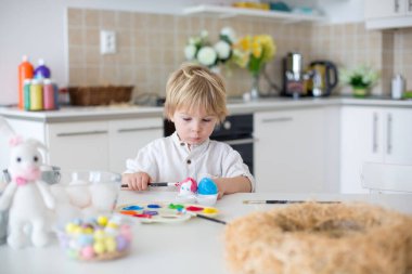 Güzel sarışın çocuk, küçük çocuk, annesiyle evde paskalya yumurtası boyuyor, gökkuşağı renginde Paskalya çelengi yapıyor.