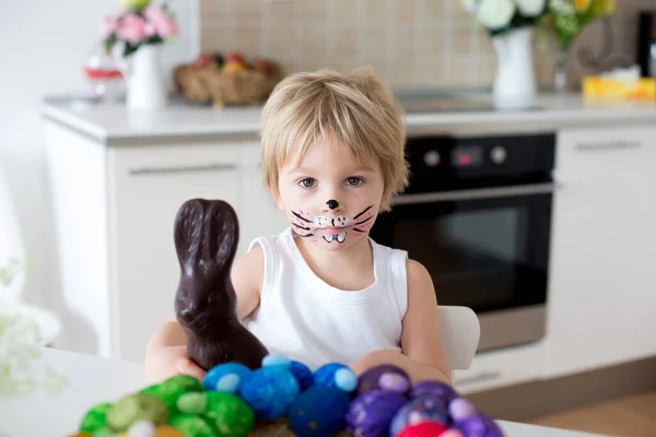 蹒跚学步的小男孩 脸上涂着兔子的孩子 在家里吃巧克力兔子 — 图库照片