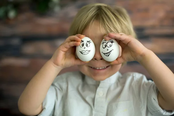 可爱的孩子 手里拿着白蛋 上面画着复活节的情感 脸上挂着滑稽的表情 — 图库照片