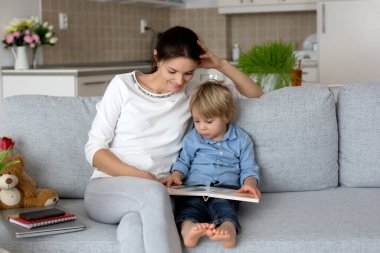 Anne, dizüstü bilgisayarı üzerinde çalışıyor ve telefonlara bakıyor. Annesi evde çalışırken yanında oynayan bir çocuk.