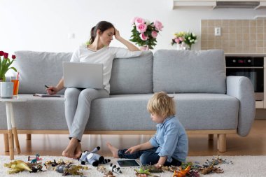 Yorgun anne, dizüstü bilgisayarı üzerinde çalışıyor, telefonlara bakıyor, çocuk evde yerde oynuyor, hem de annesi evde otururken.