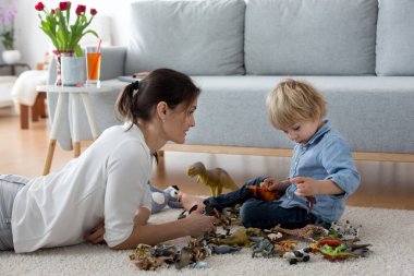 Cute blond child, toddler boy, playing at home with dinosaurs, sitting on the floor clipart