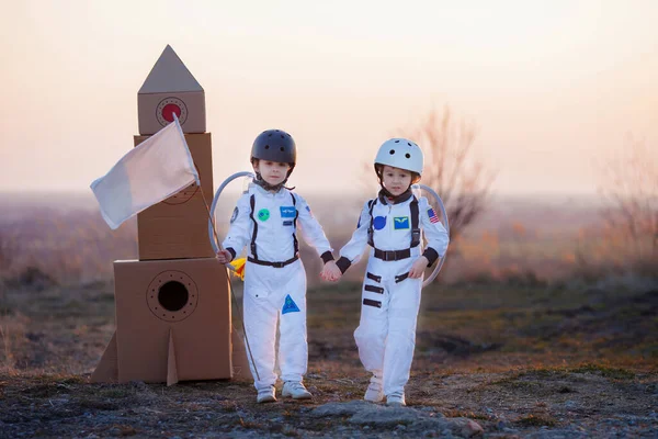 Two adorable children, boy brothers, playing in park on sunset, dressed like astronauts, imagining they are flying on the moon